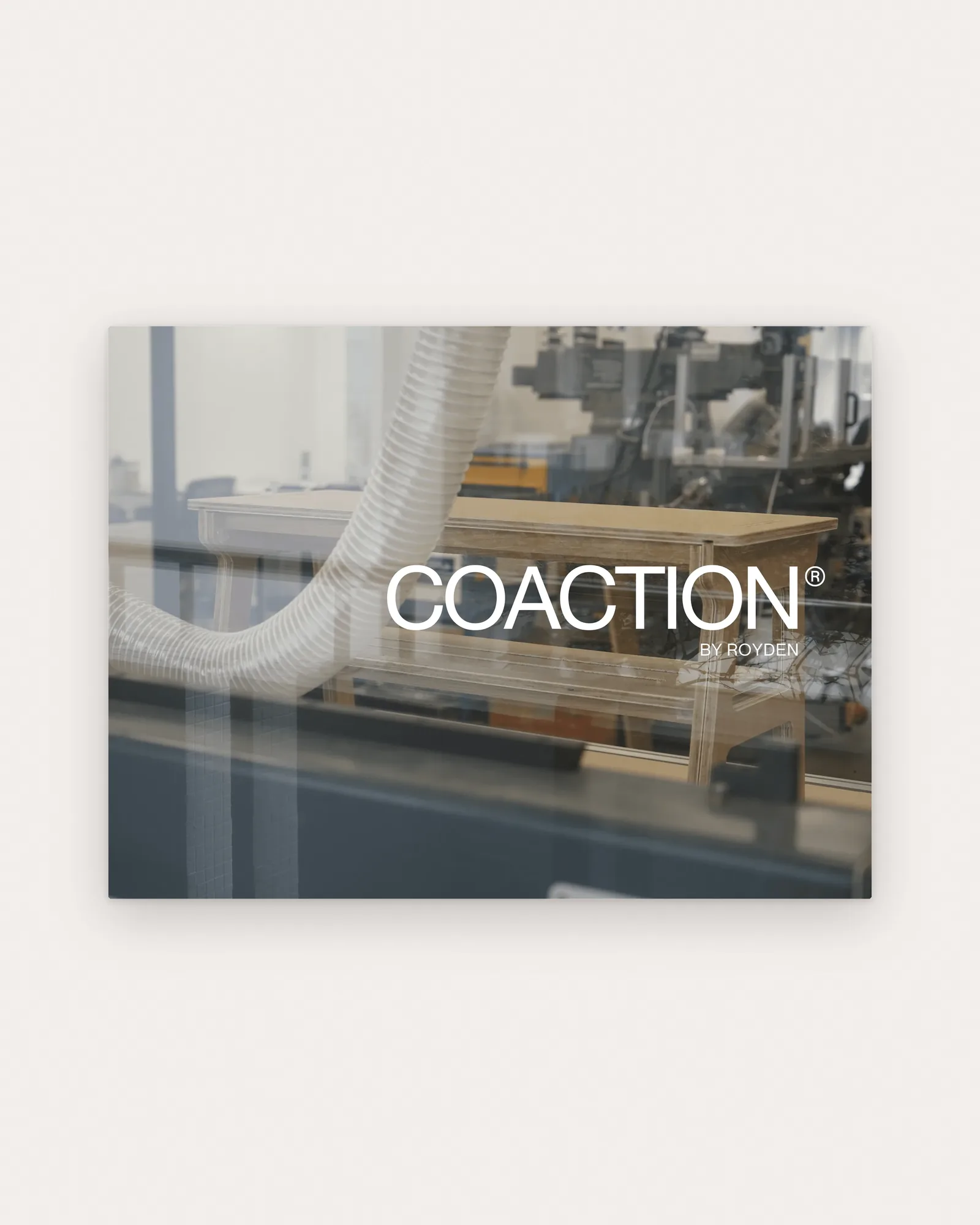 The white COACTION® BY ROYDEN wordmark over a hazy photo of the plywood shoe bench in a school workshop, seen through glass