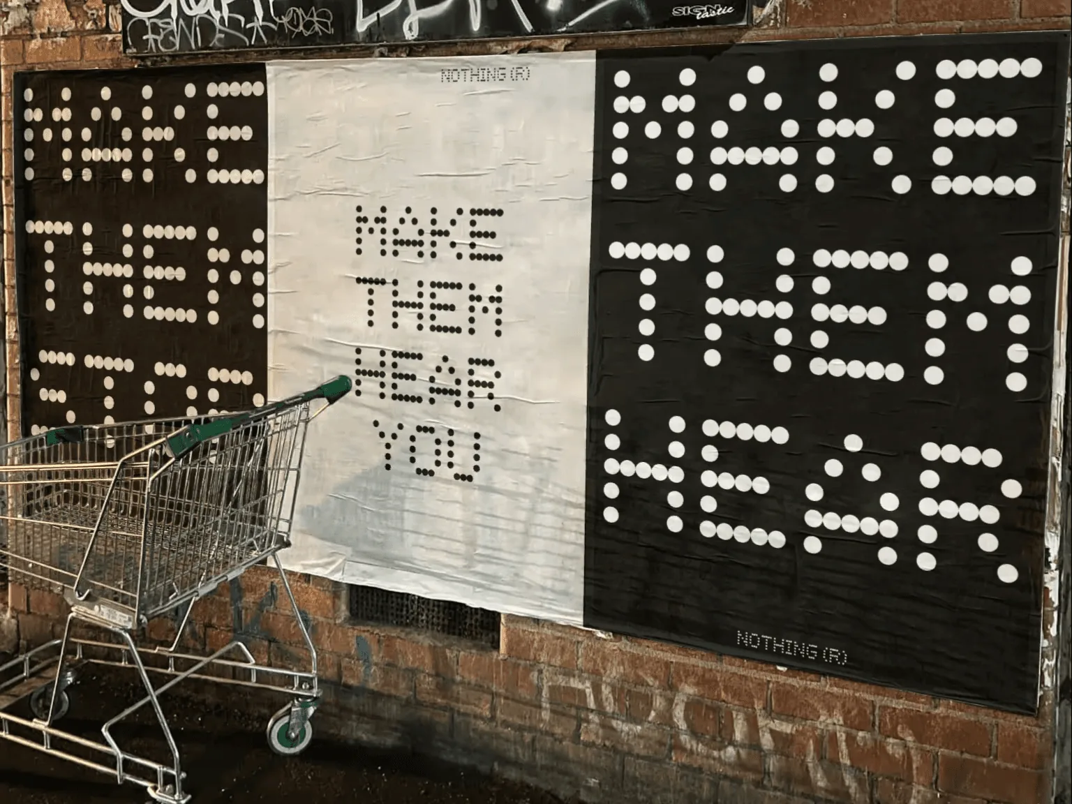 MAKE THEM HEAR YOU dot-type posters wheat-pasted on a brick wall at night