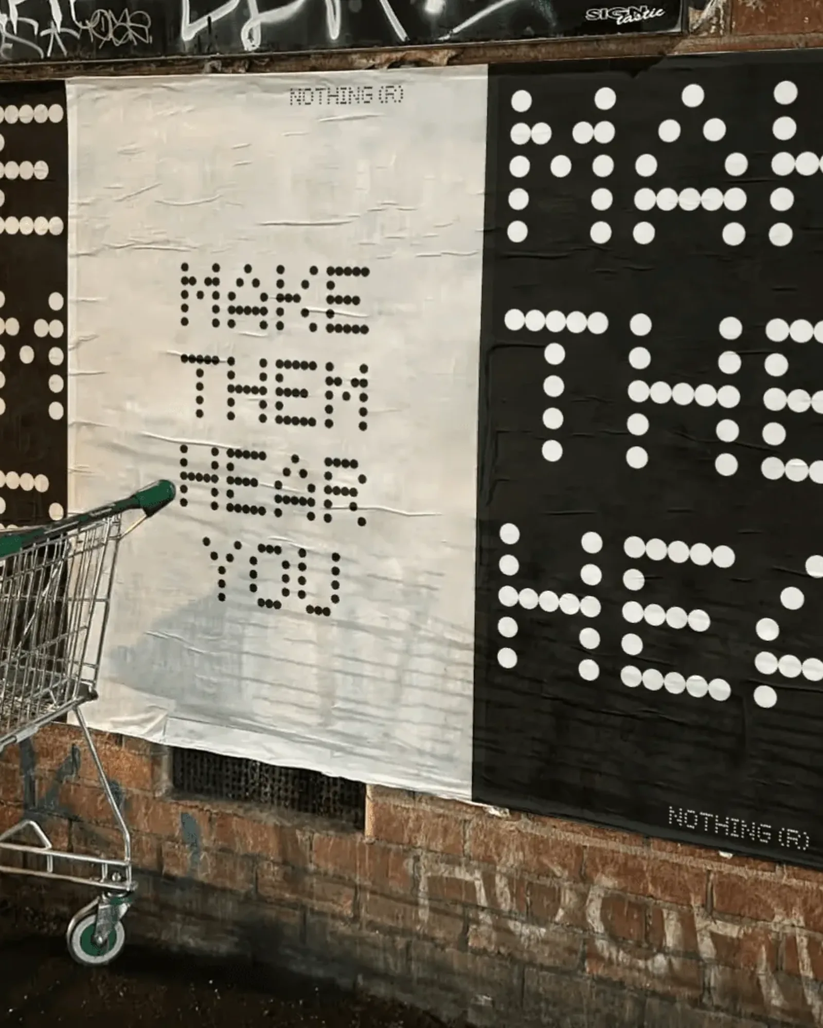 Black and white MAKE THEM HEAR YOU dot-type posters wheat-pasted on a brick wall at night, a shopping trolley in front