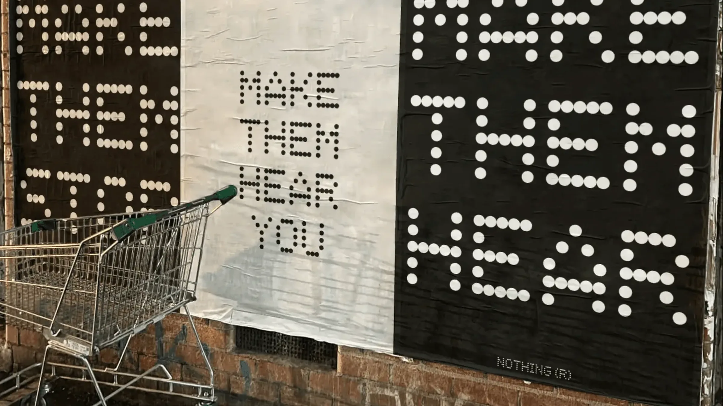 Black and white MAKE THEM HEAR YOU dot-type posters wheat-pasted on a brick wall at night, a shopping trolley in front