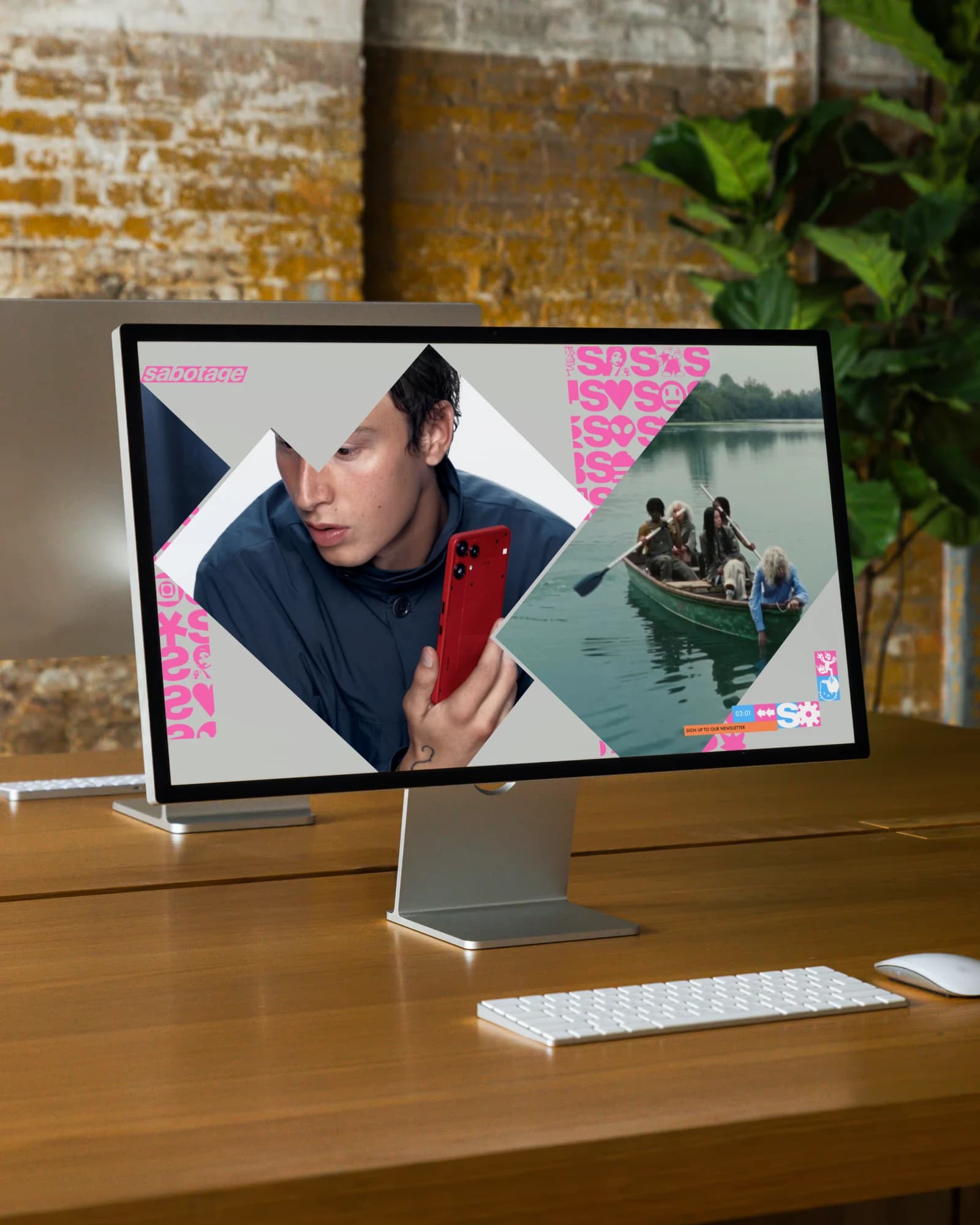 The Sabotage homepage on a Studio Display on a long wooden table against a brick wall: the pink wordmark and the strip of 45° project blocks