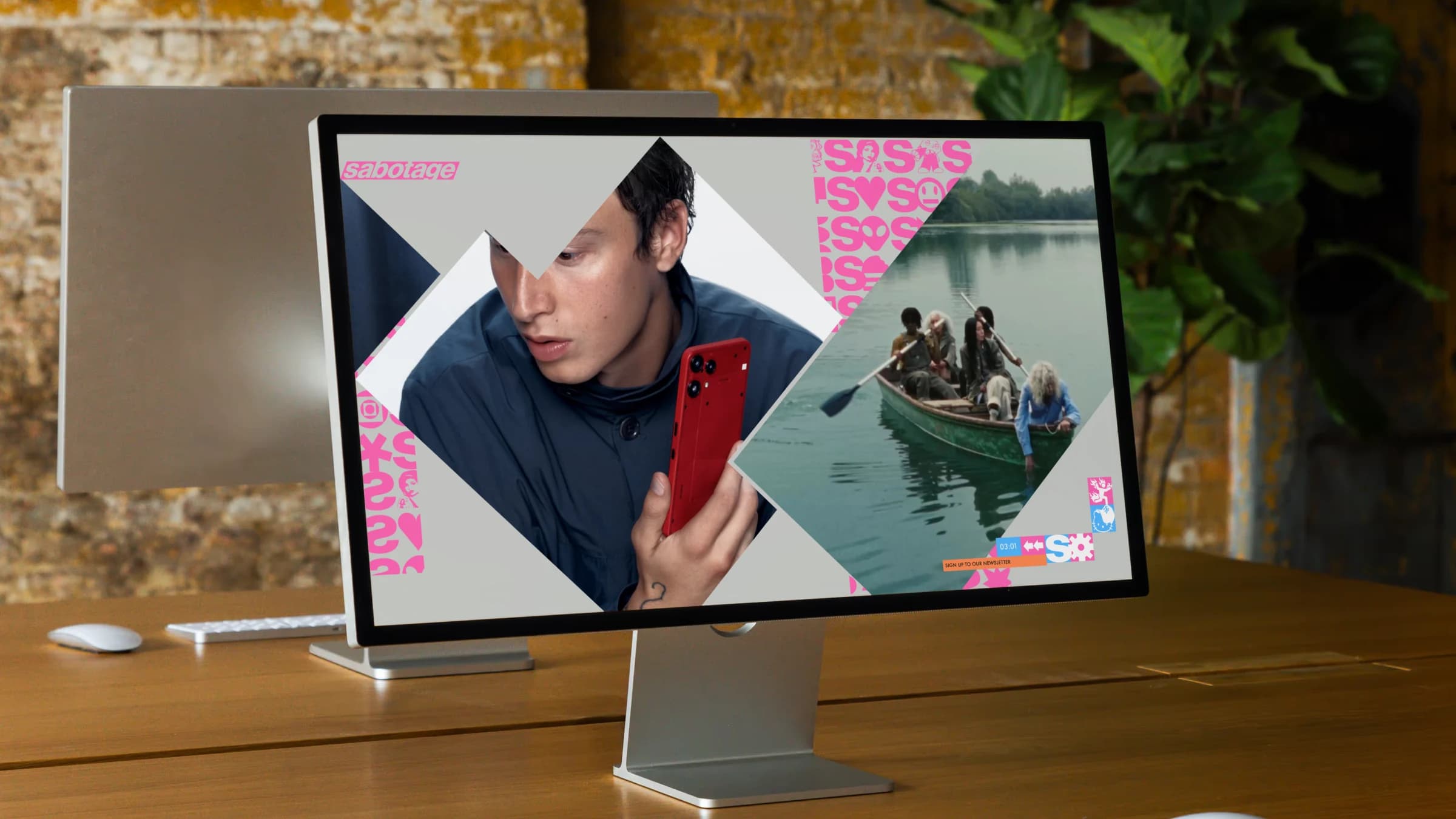 The Sabotage homepage on a Studio Display on a long wooden table against a brick wall: the pink wordmark and the strip of 45° project blocks