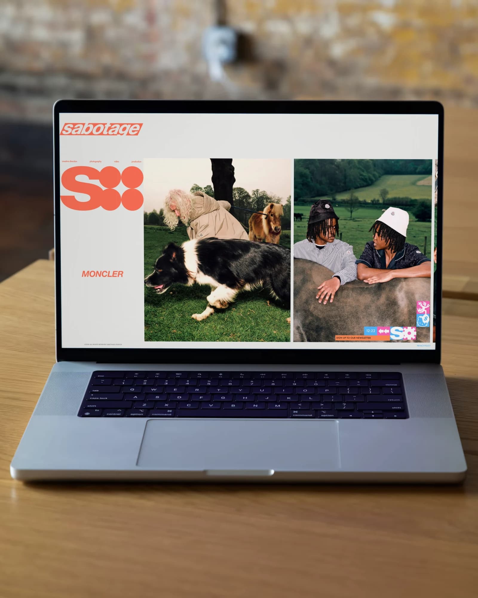 A Sabotage project page on a MacBook on a wooden desk against a brick wall: the rail with the big S, and the photographs running off to the right at one height