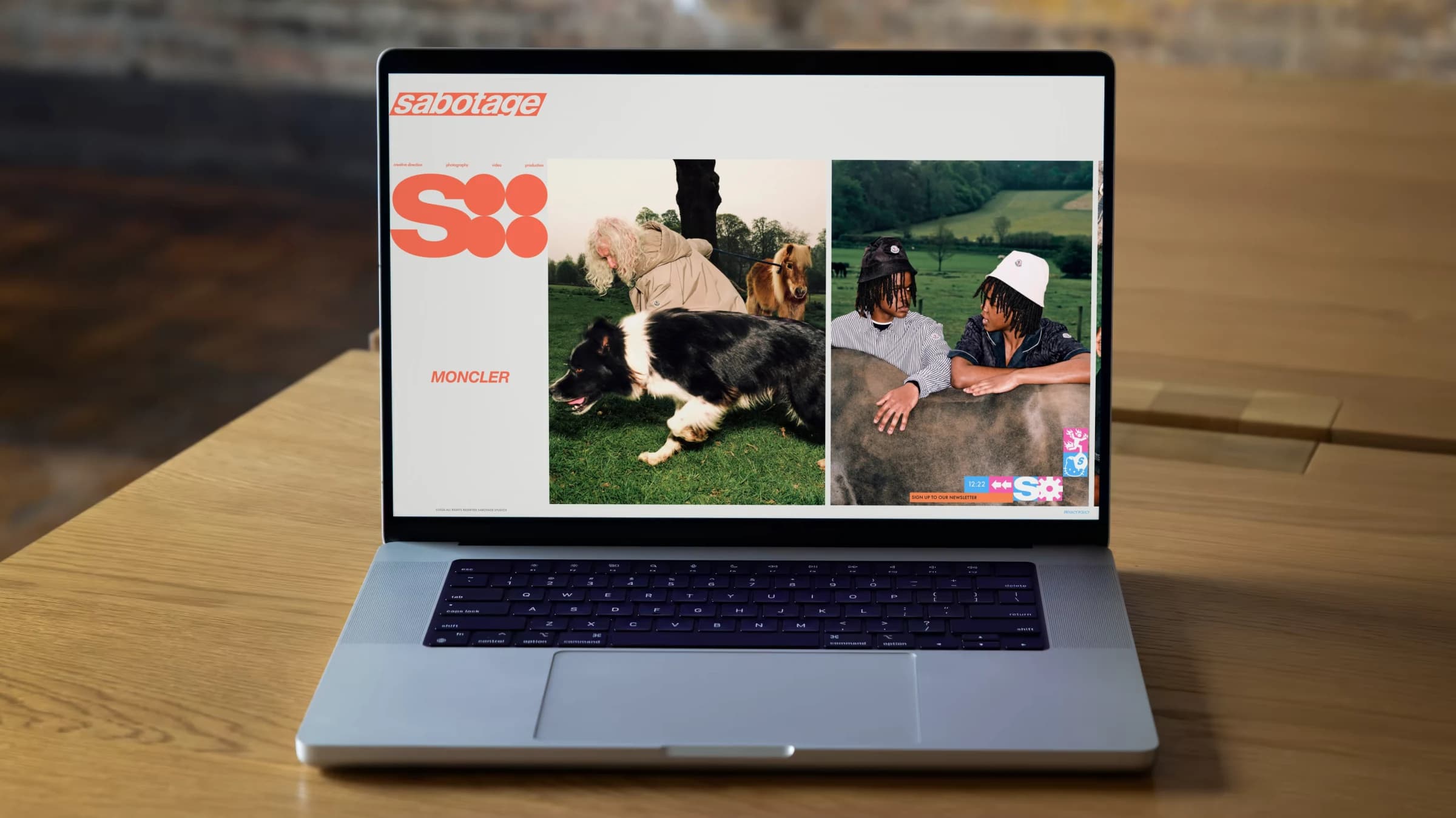 A Sabotage project page on a MacBook on a wooden desk against a brick wall: the rail with the big S, and the photographs running off to the right at one height