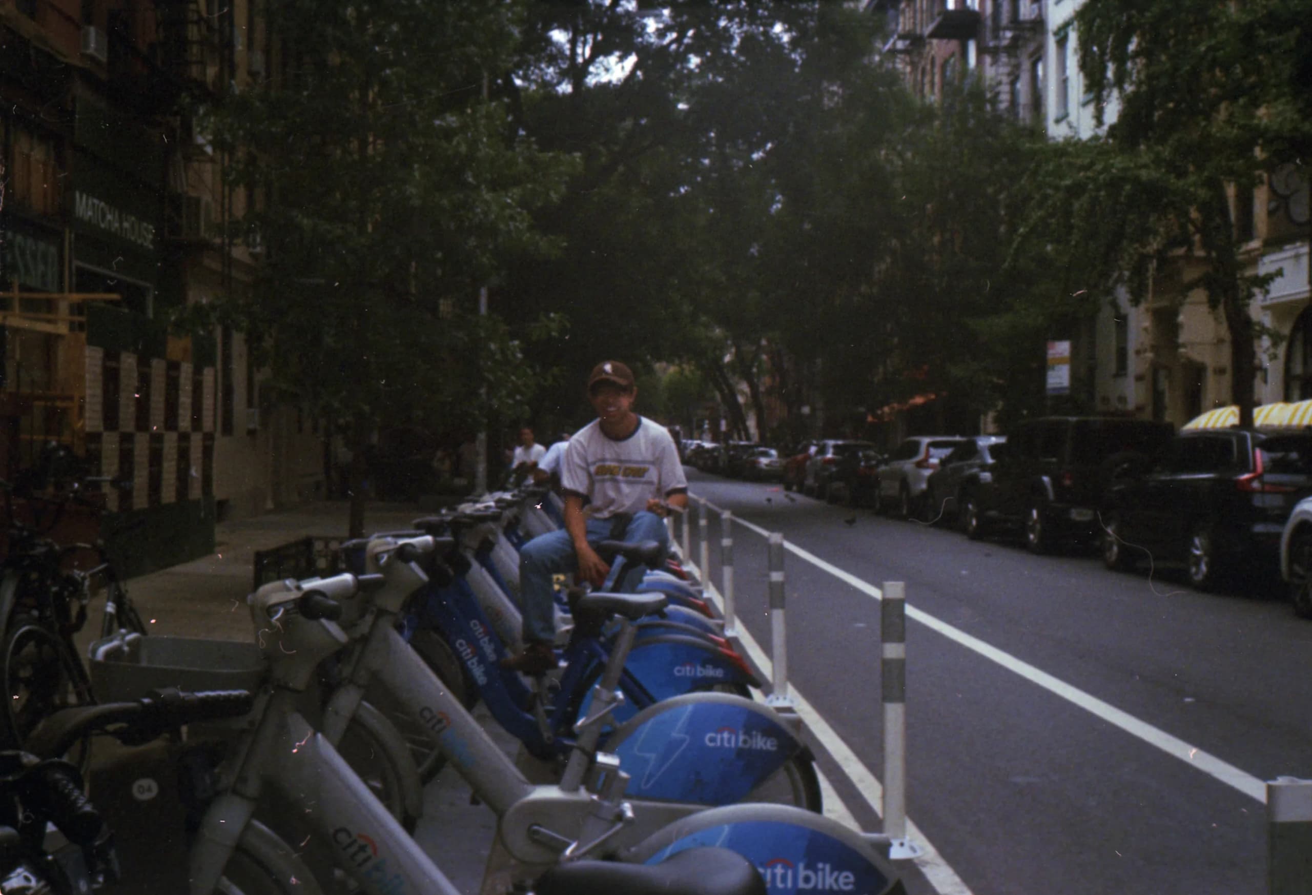 Royden sitting on a row of Citi Bikes on a tree-lined New York street, shot on film.