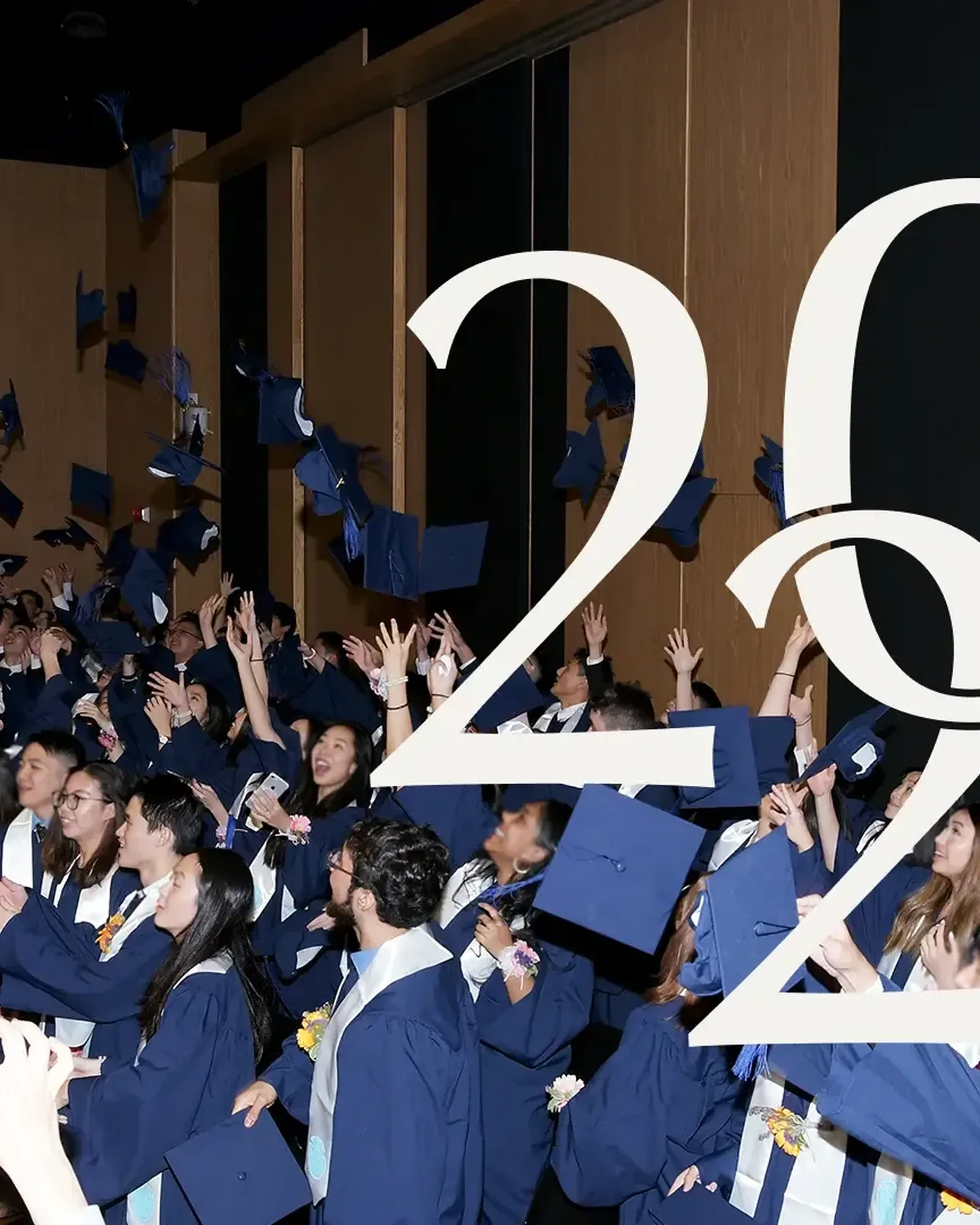 Graduates in navy gowns throwing their caps in the air, with the cream interlocking 2024 monogram over them