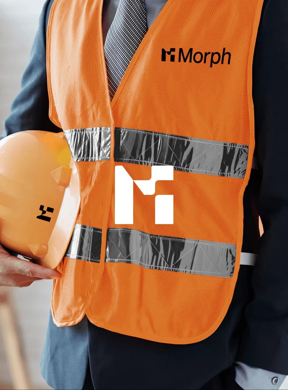 An orange hi-vis vest printed with the Morph logo and a large white M, a hard hat held beside it