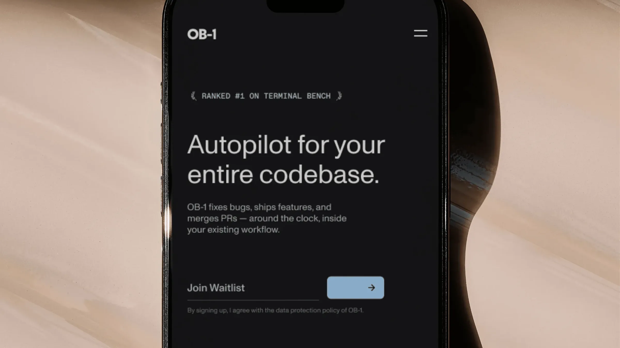 An iPhone on a glossy beige surface showing the OB-1 mobile site: Ranked #1 on Terminal Bench, Autopilot for your entire codebase, and a Join Waitlist field