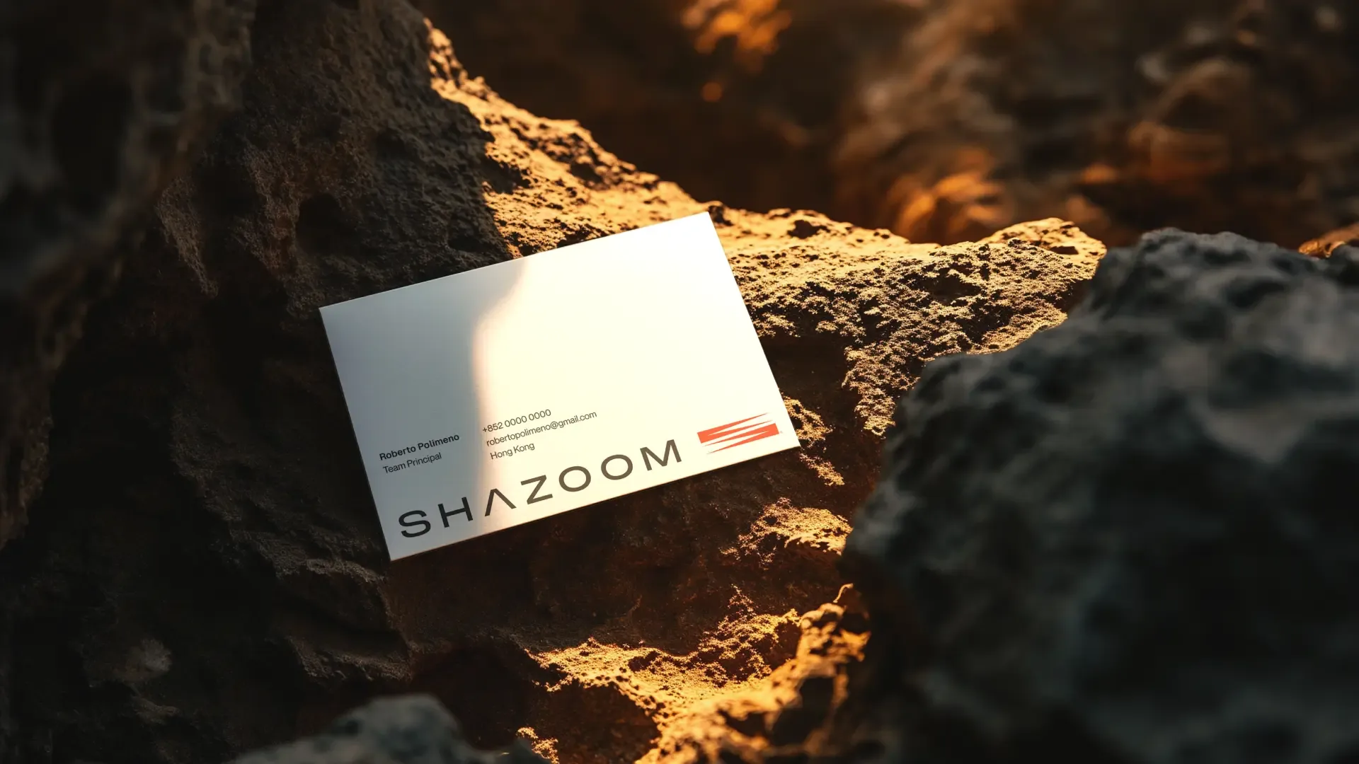 A white Shazoom business card for Roberto Polimeno, Team Principal, on sunlit volcanic rock